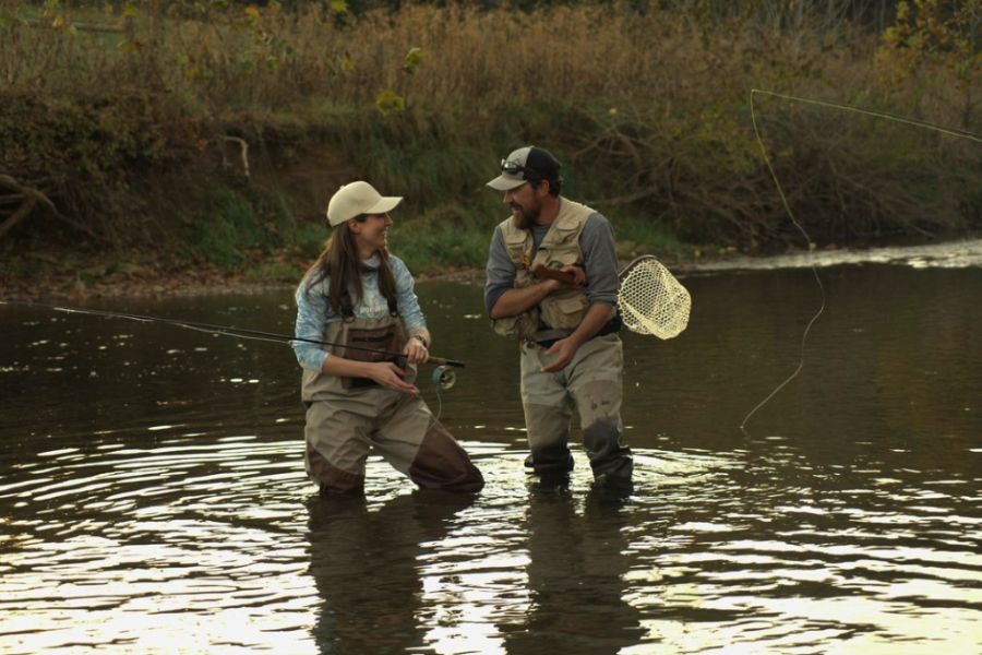 Male Shenandoah National Park fishing guide holding a net standing in the water with female angler smiling as they celebrate a great catching while near Charlottesville, VA fishing.